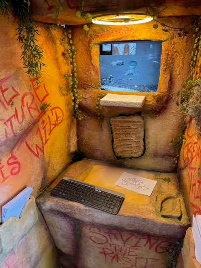 Inside the Imaginative Restoration installation --- a cave-like space with screens, a keyboard, and red spray-painted text on sandstone walls